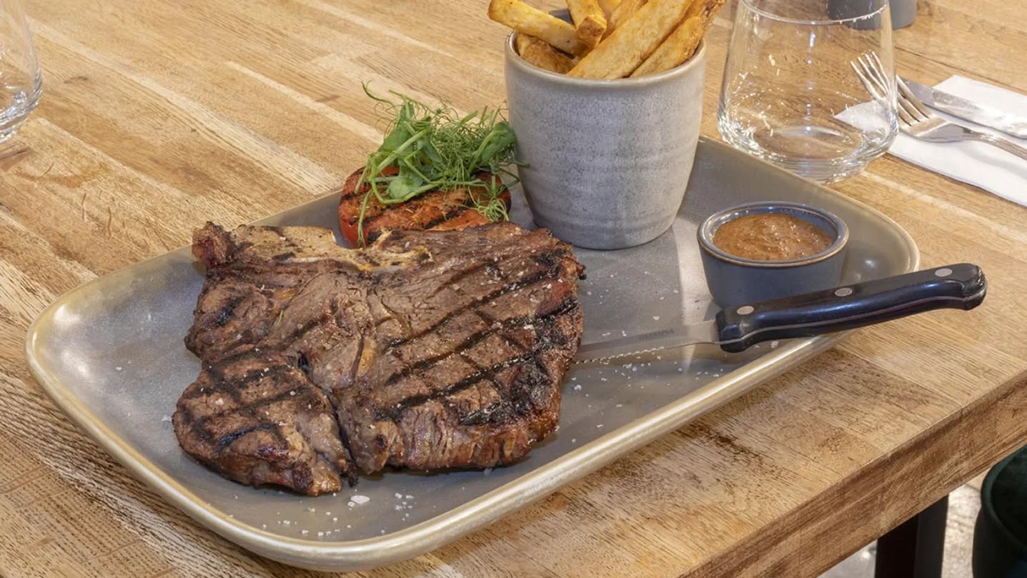 A chargrilled dry-aged T-bone steak, sliced and served with roasted tomato and herbs.
