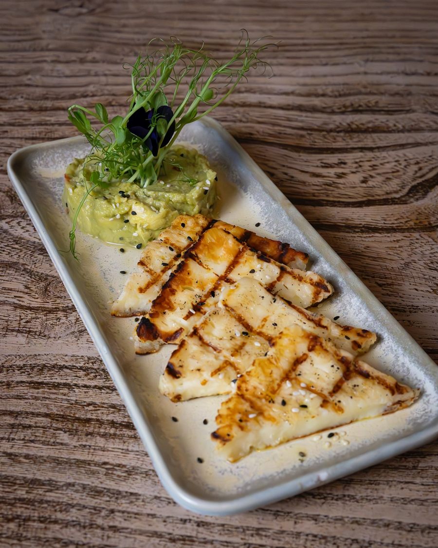 Slices of grilled halloumi over crushed avocado, topped with toasted seeds.