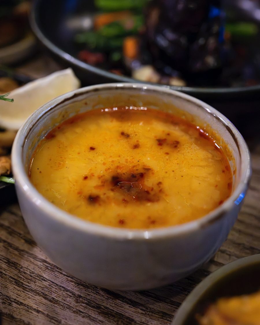 A bowl of red lentil soup finished with chilli butter, served with warm bread.