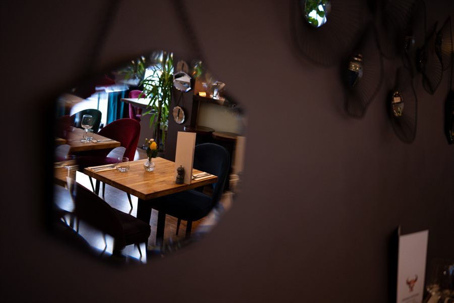 The dining room caught in a hexagonal wall mirror: tables, a yellow rose in a bud vase and velvet chairs reflected back.